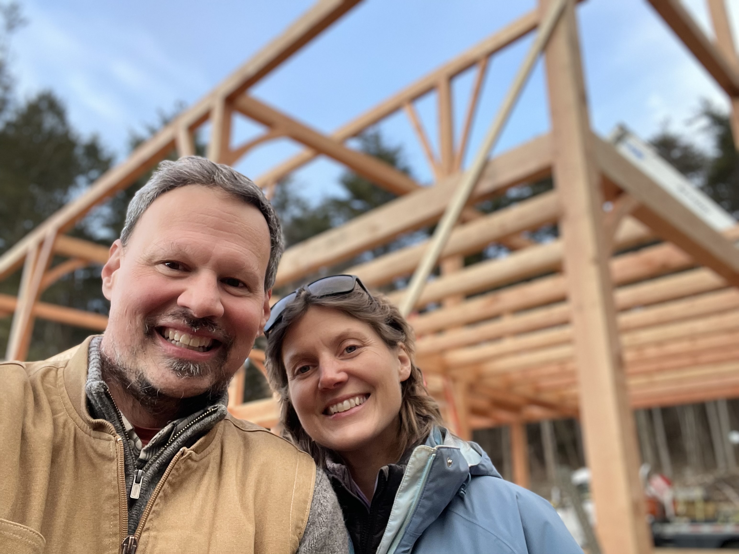 Alex and Mara Niefer, owners of Fernridge, smiling in front of a timber-frame structure under construction
